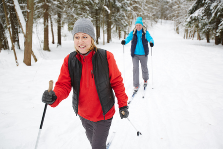 Happy mature woman in sportswear skiing with her husband in winter forestの写真素材