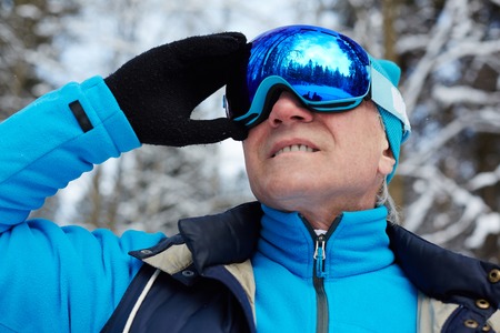 Active aged man in goggles and sportswear looking forwards in winter forestの写真素材