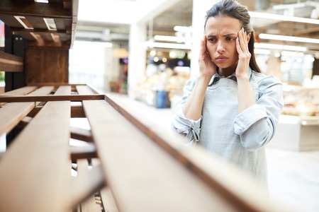 Woman feeling migraine looking at empty shelfの写真素材