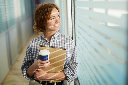 Cheerful attractive lady drinking coffee in corridorの写真素材