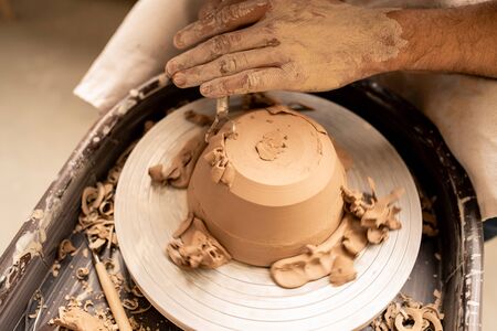 Master of pottery holding special handtool close to clay bowl to make its sides smooth during...