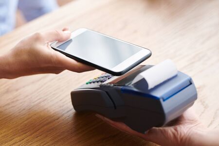 Close-up of unrecognizable customer putting smartphone to payment device while using NFC payment...