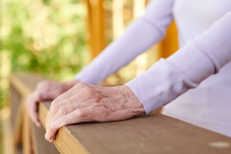 Hands of senior woman in white long-sleeved pullover holding by wooden banisters of her country house during relaxの写真素材