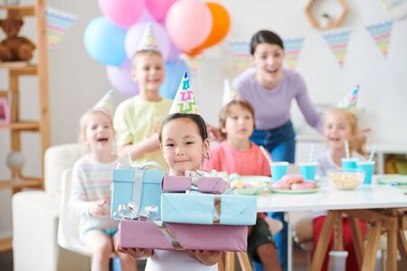 Pretty little girl in birthday cap holding stack of giftsの写真素材
