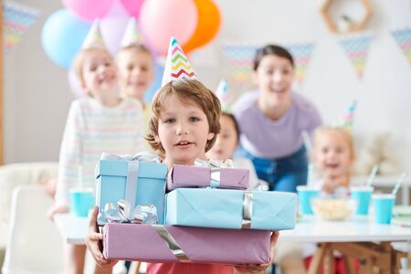 Adorable little boy in birthday cap holding pile of birthday presentsの写真素材