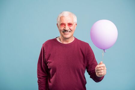 Happy retired man in pullover and eyeglasses holding balloon