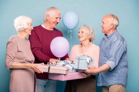 Cheerful company of friendly pensioners with balloons and giftboxes