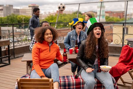 Excited girls with beer and snack chering for their football team