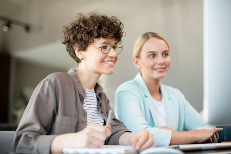 Two happy female colleagues looking at data on computer screenの写真素材