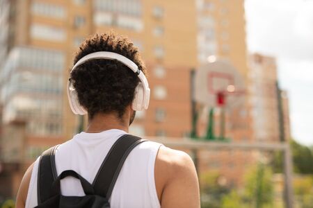 Rear view of young intercultural sportsman with headphones and backpack