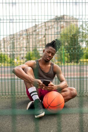 Restful African guy in sportswear scrolling or texting in smartphone