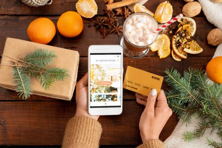 Overview of human hands with smartphone and credit card among xmas stuff
