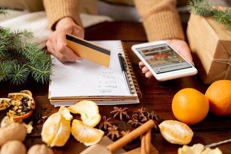 Young female customer with credit card and smartphone going to order xmas gifts