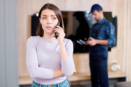Young worried woman calling her friend to consult about broken plasma panelの写真素材