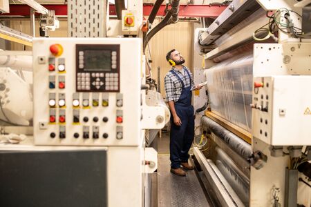Young production control engineer in workwear and protective headphones