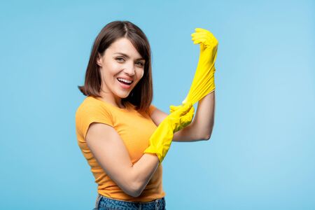 Young housekeeper putting on yellow rubber gloves before houseworkの写真素材