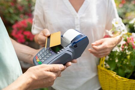 Contemporary female buyer using credit card to pay for some fresh potted flowers