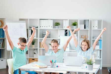 Three successful schoolmates keeping their hands raised while expressing joyの写真素材