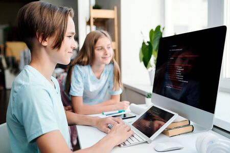 Clever boy and his classmate looking at data on computer monitorの写真素材