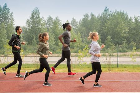Side view of four young sportsmen and sportswomen running down racetracksの写真素材