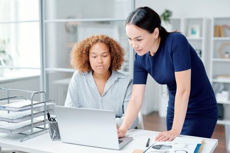 One of young businesswomen making presentation or helping colleague