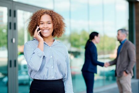 Young cheerful employee looking at you while calling on smartphoneの写真素材