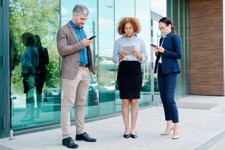 Group of young contemporary mobile employees in formalwear using gadgetsの写真素材