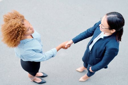 View of two multicultural businesswomen shaking hands and looking at one anotherの写真素材
