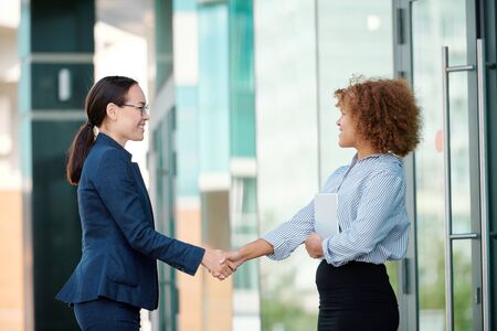 Two young successful female colleagues welcoming one another by handshakeの写真素材