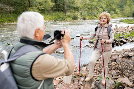Mature woman with trekking sticks posing for camera held by her husband
