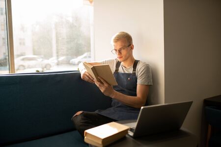 Serious young worker of cafeteria reading books about restaurant business