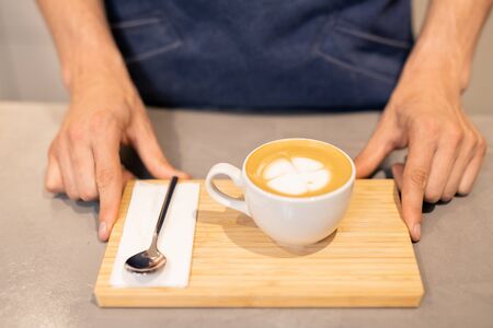 Porcelain cup of cappuccino and small spoon with paper napkin on wooden trayの写真素材