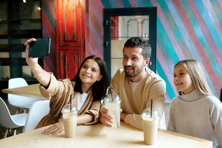 Young cheerful family of three resting by table in cafe after shoppingの写真素材