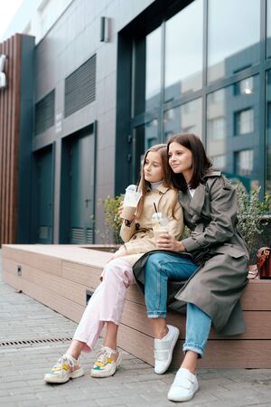 Two restful females in smart casual having drinks while relaxing outdoorsの写真素材