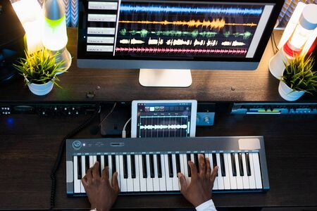 Top view of human hands on keys of piano keyboard during process of recording new music and mixing...