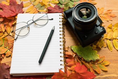 Photocamera, blank page of copybook with eyeglasses and pen and autumn leavesの写真素材