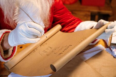 Gloved Santa holding pen over big paper with list of kids namesの写真素材