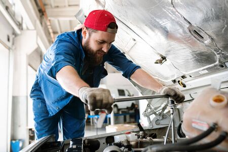 Young technician in workwear bending over engine of car or lorry