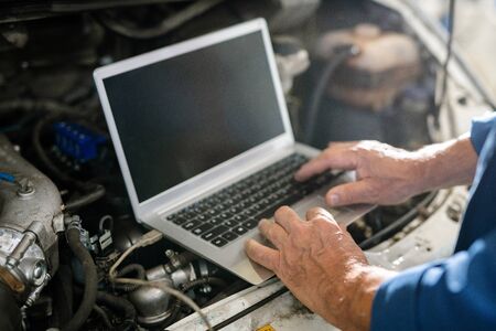 Hands of mature master of car repair service over keyboard of laptopの写真素材