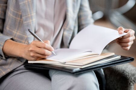 Young school teacher with pen correcting mistakes or putting mark in copybook