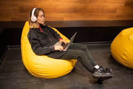 Pretty young restful woman in casualwear listening to music in headphones
