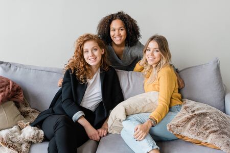 Group of friendly intercultural girls in smart casual sitting on sofaの写真素材