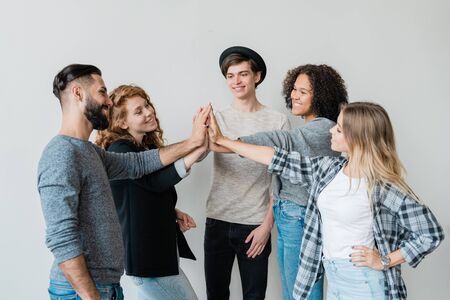 Group of young intercultural friends in casualwear making high-fiveの写真素材