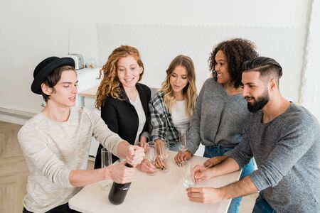 Group of young friends with flutes looking at guy opening bottle of champagneの写真素材