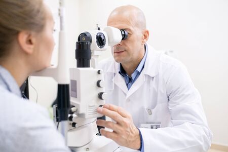 Middle aged professional optometrist checking eyesight of female patient while using new medical...