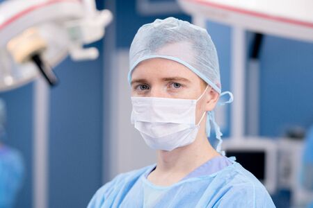 Young intern or surgeon in protective mask and uniform looking at you