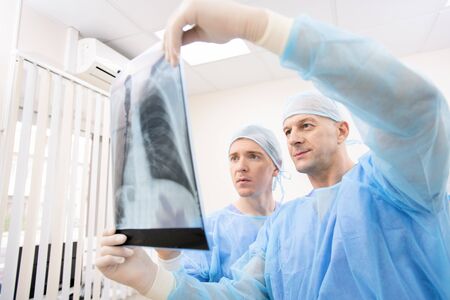 Young and mature doctors in uniform looking attentively at x-ray of lungs