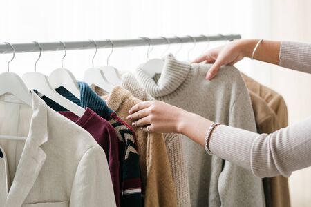 Hands of young female shopper choosing warm knitted and woolen clothes from new seasonal casualwear...
