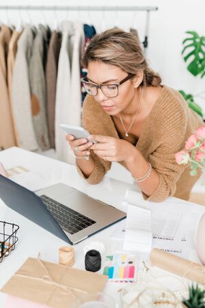 Pretty young casual shop assistant of modern boutique bending over workplaceの写真素材