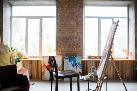 Wooden chair of painter, easel with unfinished painting, various equipment for art working inside...